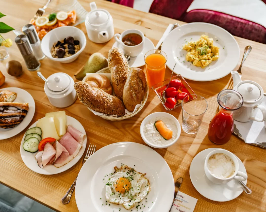Ein reich gedeckter Frühstückstisch mit allerhand Leckereien wie frischem Gebäck, Schinken, Wurst, Käse, Gemüse, Eierspeise, Spiegelei und Müsli.