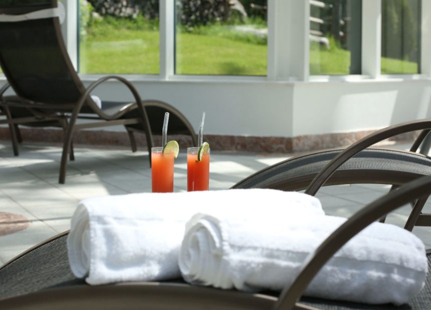 Zwei orangefarbene Cocktails mit einer Limettenscheibe stehen auf einer Liege im Wellnessbereich des Wellnesshotels Lärchenhof, hinter zwei aufgereihten weißen Handtüchern.