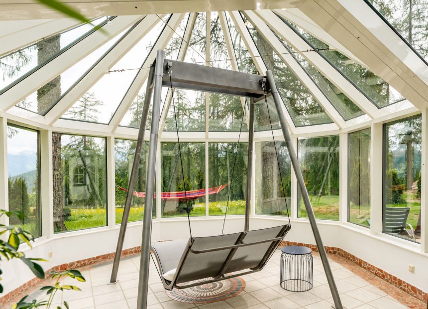 Eine schwingende Schaukelliege unter großen Glasflächen des Wellnessbereichs mit Blick ins Grüne erwartet im Naturhotel Lärchenhof
